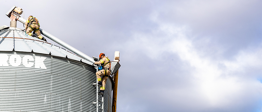 Two firefighters climbing to the top of a grain bin