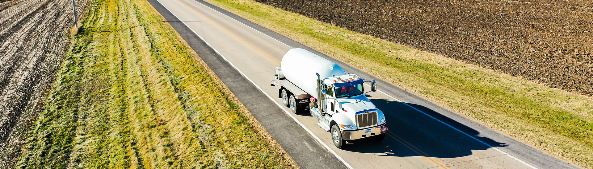 Propane delivery truck on open road between fields